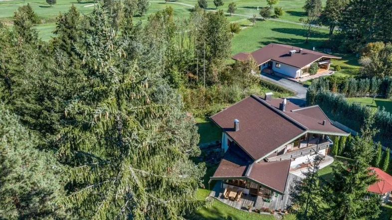 Luftaufnahme von zwei Häusern mit braunen Dächern, umgeben von grünen Bäumen und einem Golfplatz.