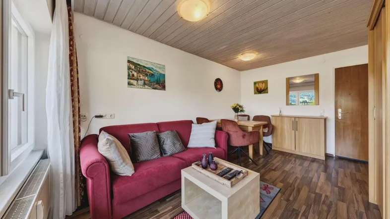 Gemütlicher Wohn-Essbereich mit rotem Sofa, Holzboden und Holzdeckenverkleidung.