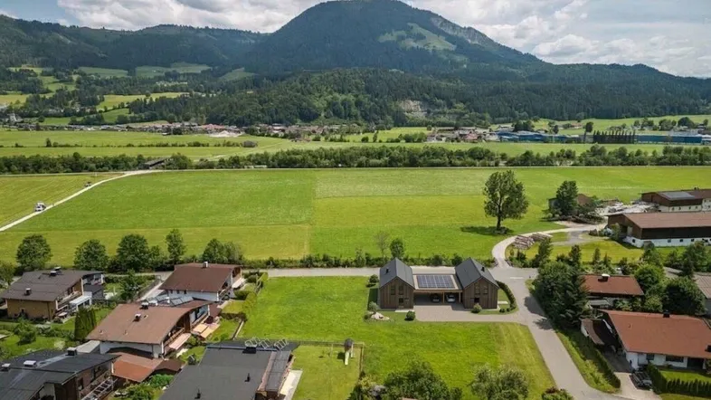 Luftaufnahme eines modernen Hauses mit Photovoltaikanlage in ländlicher Umgebung und Bergblick.
