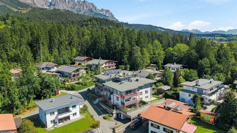 Luftaufnahme eines modernen Wohngebäudes in alpiner Umgebung mit Bergblick und viel Grün.