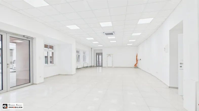 Heller, weitläufiger Gewerberaum mit großen Fenstern, weißen Fliesen und moderner Deckenbeleuchtung, bereit zur Nutzung.