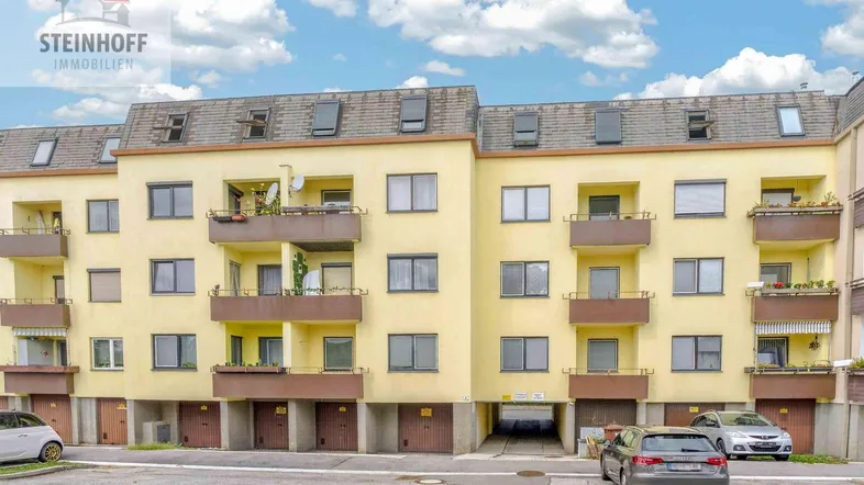 Mehrfamilienhaus mit Balkonen, Dachfenstern und Garagen im Erdgeschoss.