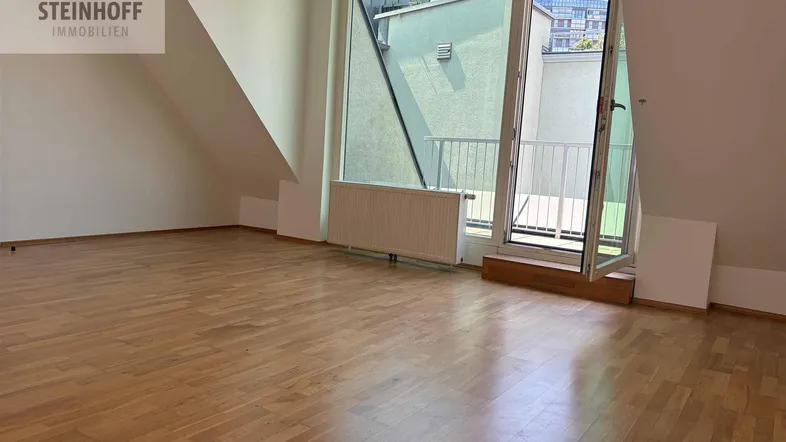 Heller Raum mit Holzparkettboden, Dachschrägen und Zugang zu einem Balkon oder einer Terrasse.