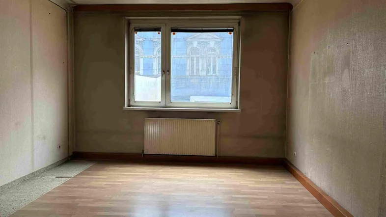Leeres Zimmer mit Holzparkettboden und Fenster, das auf ein Gebäude blickt, bereit zur Renovierung.