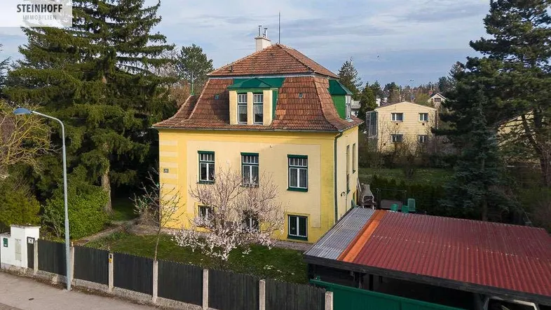 Historisches gelbes Einfamilienhaus mit Mansarddach und gepflegtem Garten in grüner Umgebung.
