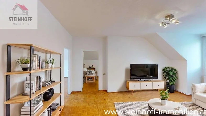 Helles Wohnzimmer mit Parkettboden, Dachschrägen und Blick in einen weiteren Raum.
