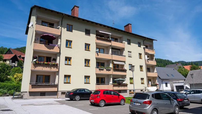 Mehrfamilienhaus mit mehreren Balkonen und Außenparkplätzen unter blauem Himmel.