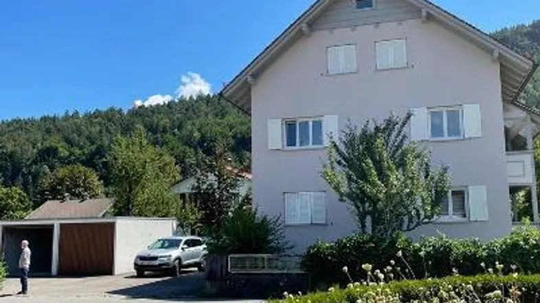 Helles Mehrfamilienhaus mit Satteldach, Garage und gepflegter Auffahrt in grüner Umgebung.