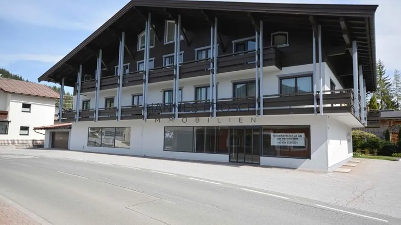 Mehrstöckiges Gebäude mit traditioneller Architektur, Balkonen und Geschäftsflächen im Erdgeschoss an einer Straße.