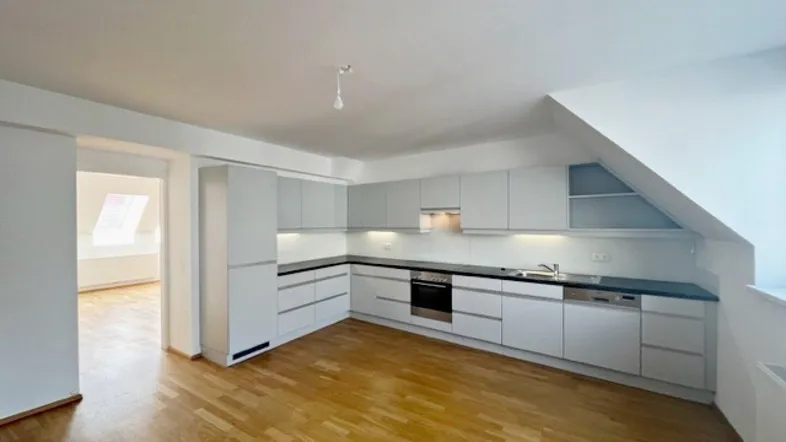 Moderne Einbauküche in hellem Raum mit Holzparkett und Dachschräge, offen zu einem weiteren Zimmer.
