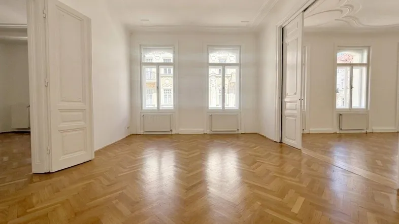 Geräumiges Wohnzimmer in einem Altbau mit Fischgrätparkett, hohen Decken und Stuckverzierungen.
