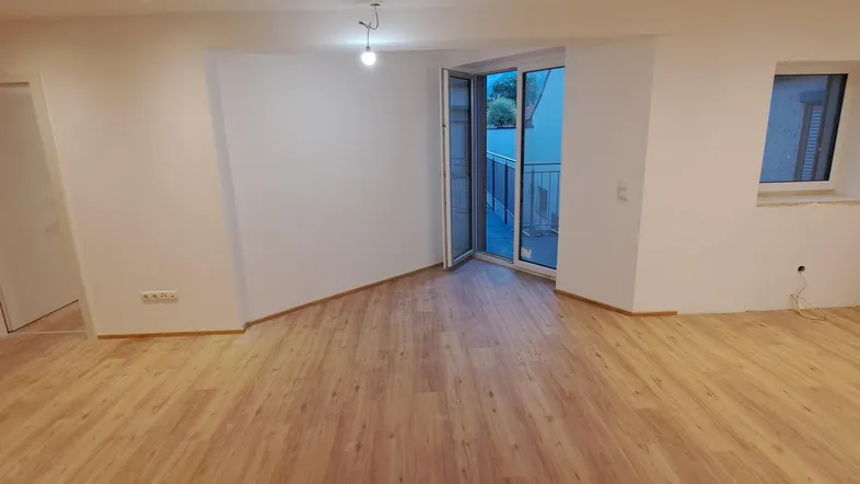 Heller Wohnbereich mit neuem Laminatboden und Zugang zu einem kleinen Balkon.