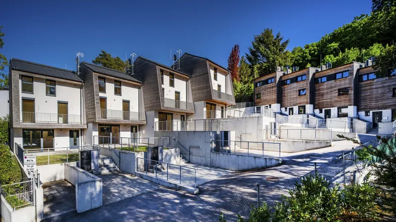 Moderne Reihenhäuser mit Holzfassaden und Balkonen in einer grünen Umgebung.