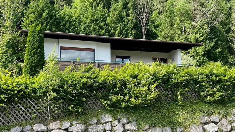 Modernes Haus mit weißer Fassade, umgeben von üppiger grüner Vegetation und einem Steinsockel.