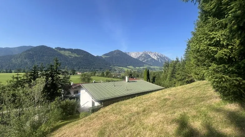 Haus in alpiner Landschaft mit grüner Umgebung und Bergblick unter blauem Himmel.