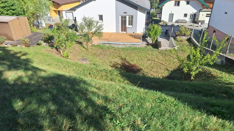 Blick auf das Haus von hinten mit einer neuen Holzterrasse und einem großen, abfallenden Garten.