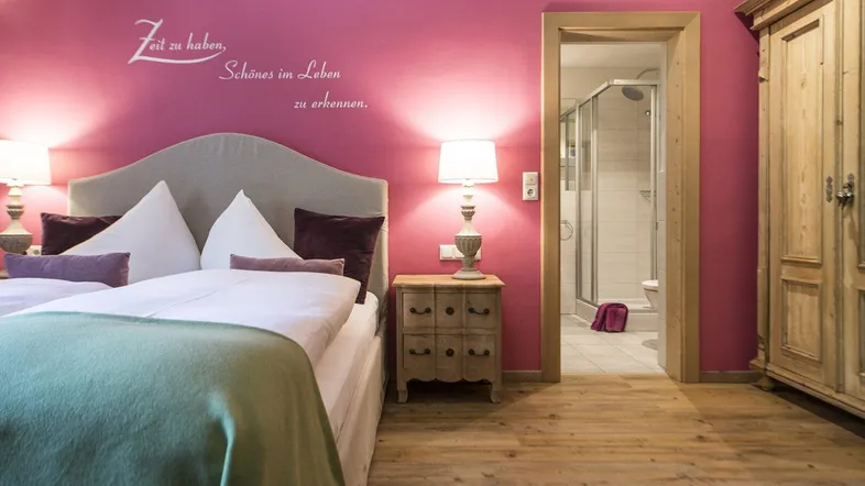 Schlafzimmer mit pinker Wand, Holzboden und Zugang zu einem Badezimmer.