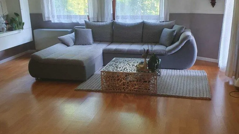 Helles Wohnzimmer mit gemütlichem Ecksofa, Holzboden und Blick ins Grüne.