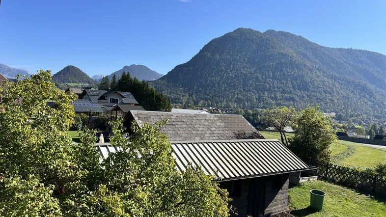 Bergblick mit grüner Landschaft und traditionellen Häusern unter blauem Himmel.