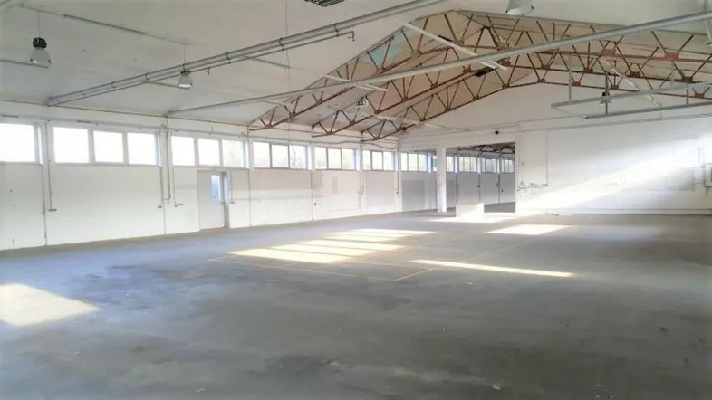 Große, leere Industriehalle mit hohen Decken, Betonboden und viel Tageslicht durch Fensterreihen.