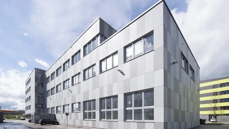 Modernes Bürogebäude mit gestreifter Fassade und vielen Fenstern unter bewölktem Himmel.