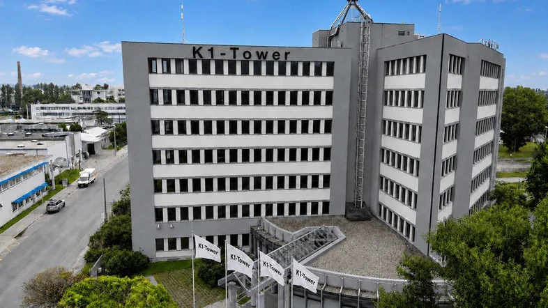 Blick auf den K1-Tower, ein modernes Bürogebäude mit grauer Fassade und vielen Fenstern, umgeben von Grünflächen.