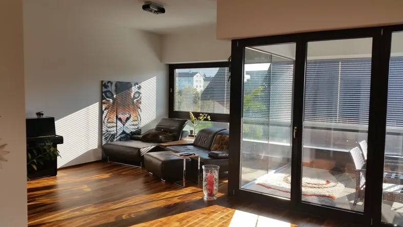 Helles Wohnzimmer mit Holzboden, bequemen Sitzmöbeln und Zugang zu einem verglasten Balkon.
