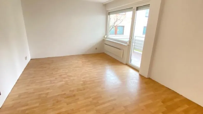 Helles Zimmer mit Parkettboden und Zugang zu einem kleinen Balkon.