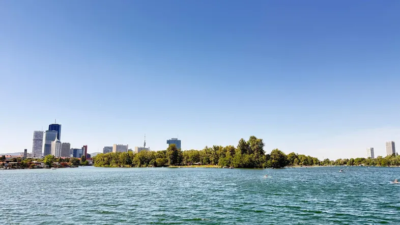 Panoramablick über den See mit einer beeindruckenden Stadtsilhouette am Horizont unter klarem Himmel.