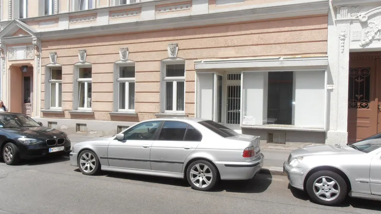 Ansicht der Gebäudefassade eines Altbaus mit geparkten Autos auf der Straße an einem sonnigen Tag.