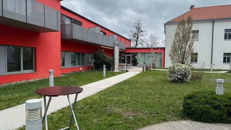 Außenansicht eines Gebäudes mit roter Fassade, gepflasterten Wegen und Grünflächen im Innenhof.