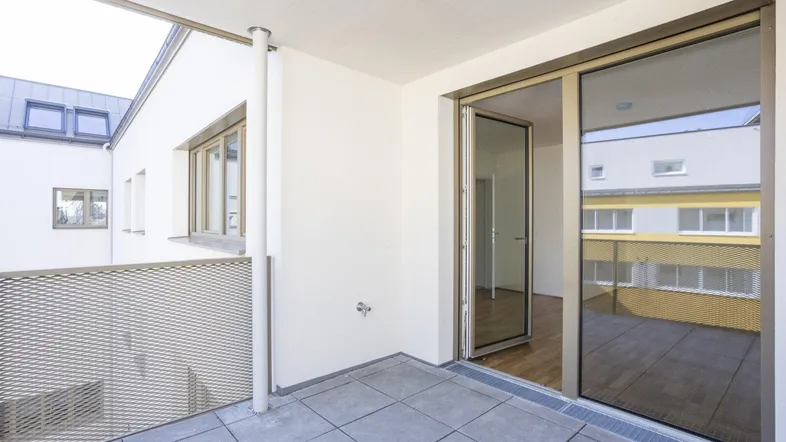 Geräumiger Balkon mit grauen Fliesen und Metallgeländer, bietet Blick auf umliegende Gebäude.