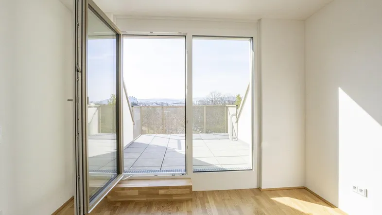 Helles Zimmer mit Holzboden und Zugang zu einer großen Terrasse mit Weitblick.