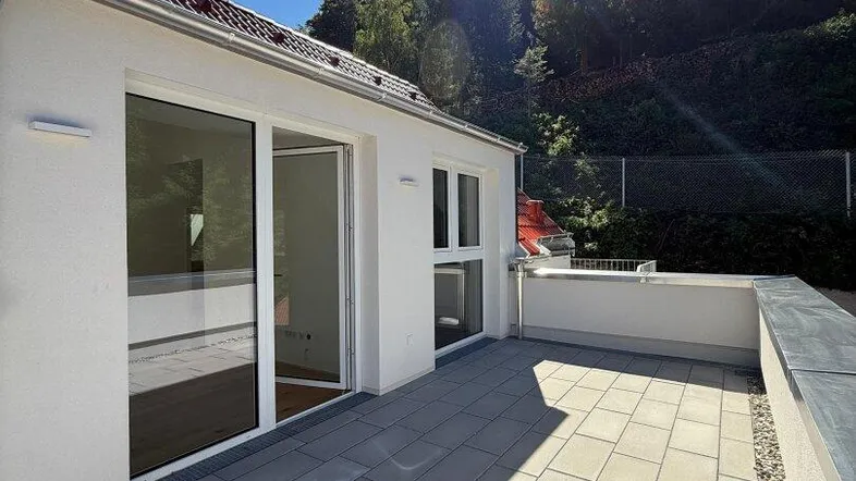 Sonnige Terrasse mit modernen Fliesen und Zugang zum Innenbereich, umgeben von grünen Bäumen.