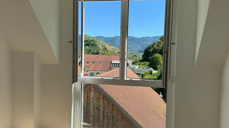 Helles Zimmer im Dachgeschoss mit Holzboden und weitem Blick auf die Weinberge und Berge.