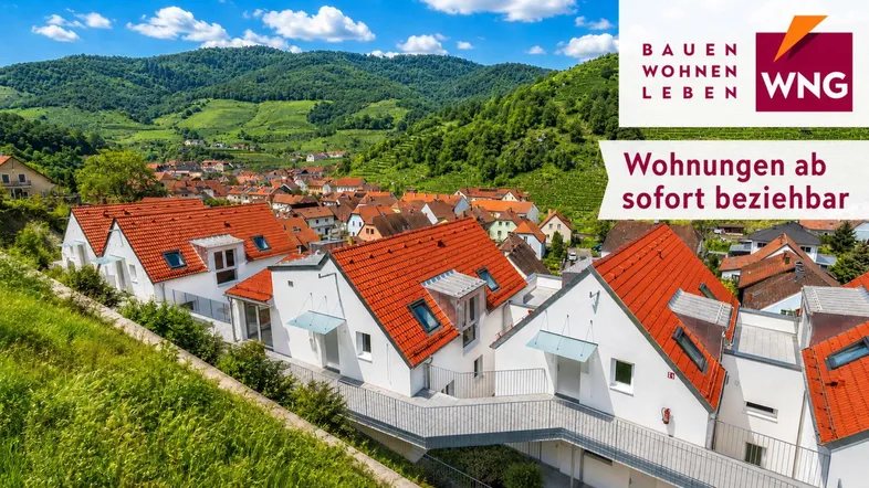 Moderne Reihenhäuser mit roten Ziegeldächern in Hanglage, umgeben von grünen Hügeln und einem Dorf.