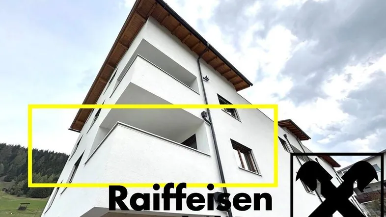 Modernes Mehrfamilienhaus mit weißer Fassade und Balkonen, eingebettet in eine grüne Berglandschaft.