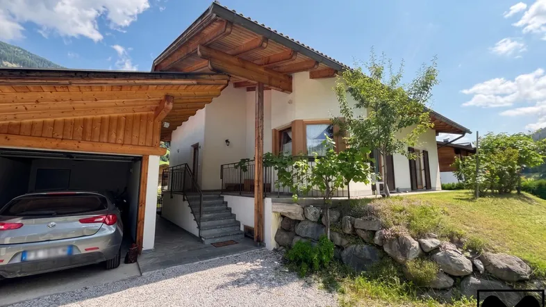 Hausfassade mit Holzelementen, Carport und gepflegtem Vorgarten in ländlicher Umgebung.