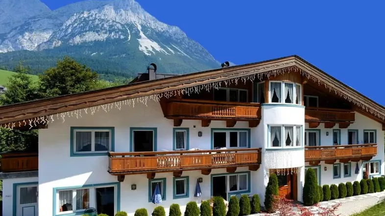 Traditionelles Alpenhaus mit Holzbalkonen und beeindruckendem Bergblick unter blauem Himmel.