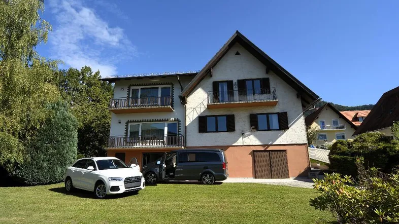 Großes Einfamilienhaus mit Satteldach, Balkonen und gepflegtem Vorgarten, umgeben von Bäumen.
