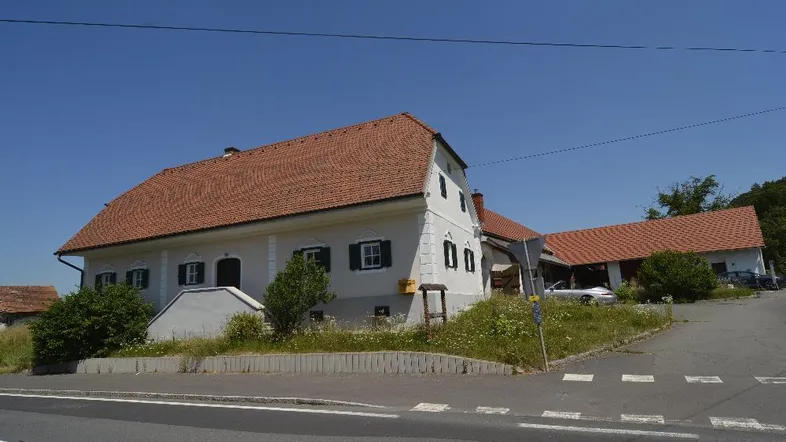 Weißes Landhaus mit rotem Ziegeldach und grünen Fensterläden an einer ländlichen Straße.