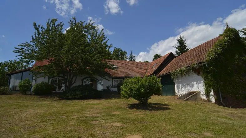 Ländliches Anwesen mit weißer Fassade, Ziegeldach und umgebender Natur unter blauem Himmel.