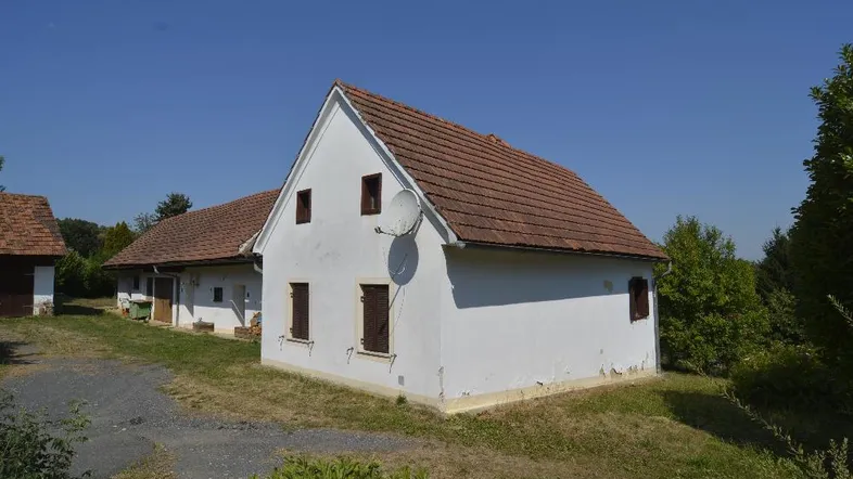 Weißes Landhaus mit Satteldach und Satellitenschüssel in ländlicher Umgebung unter blauem Himmel.