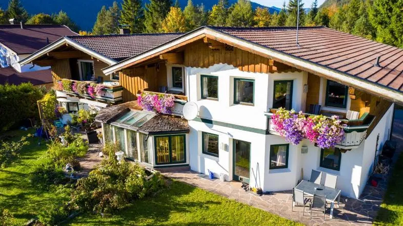 Traditionelles Alpenhaus mit blumengeschmückten Balkonen, Garten und Bergblick unter blauem Himmel.