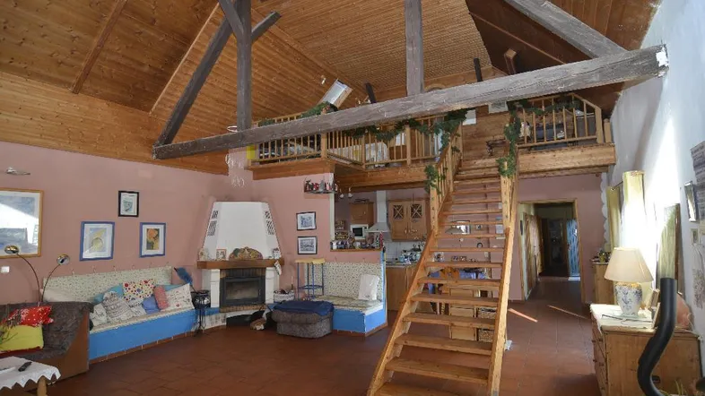 Geräumiges Wohnzimmer mit Holzbalken, Kamin und offener Galerie, die eine gemütliche Atmosphäre schafft.