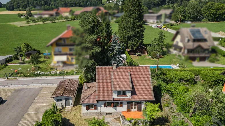Luftaufnahme eines Hauses mit rotem Ziegeldach, umgeben von grünen Feldern und Bäumen, mit einem Parkplatz.