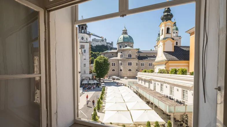 Blick aus einem Fenster auf eine historische Stadtlandschaft mit beeindruckenden Gebäuden und einem belebten Platz.