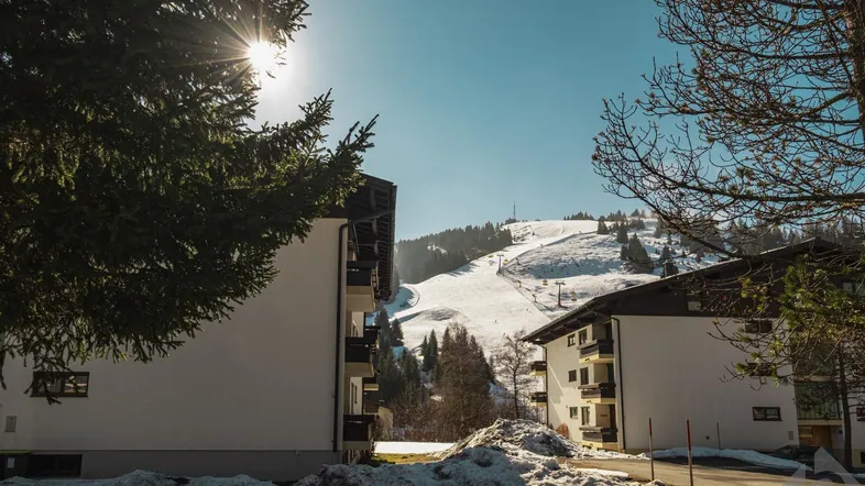Winterlandschaft mit verschneiten Bergen und Gebäuden, die einen Skihang überblicken.