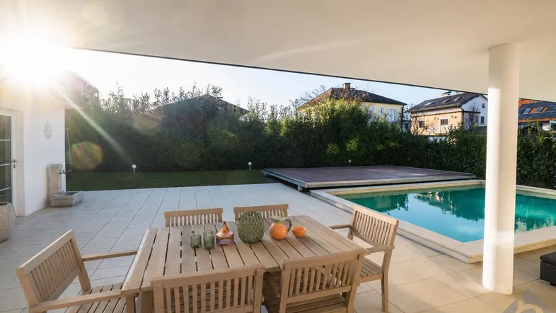 Sonnige Terrasse mit Esstisch und Stühlen, direkt am Pool gelegen, ideal für Mahlzeiten im Freien.