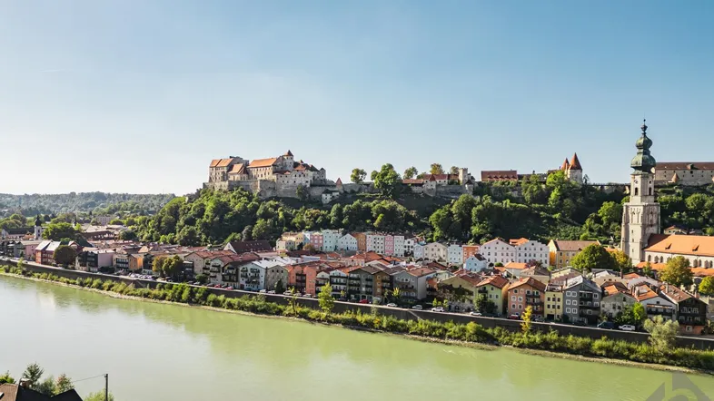 Panoramablick auf eine historische Stadt am Fluss mit einer imposanten Burg auf dem Hügel.